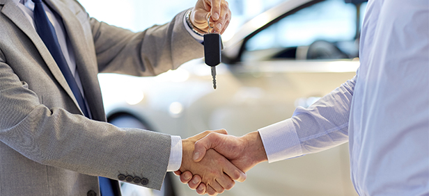 two people shaking hands while one hand over new car keys to the other.
